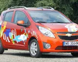 Pomarańczowy Chevrolet Spark z kolorowymi, abstrakcyjnymi wzorami na karoserii.
