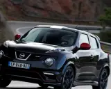 Czarny Nissan Juke Nismo z czerwonymi lusterkami i białym pasem na dachu pędzi po krętej drodze.