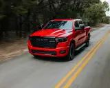Czerwony Dodge Ram 1500 5.7 Hemi pędzi po krętej drodze wśród drzew.