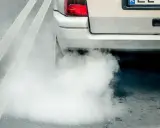 Z rury wydechowej wydobywa się gęsty, biały dym, tworząc chmurę na drodze.