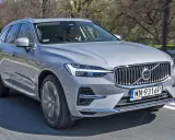 Srebrny Volvo XC60 2025 w ruchu, z kierowcą za kierownicą, na tle drzew.