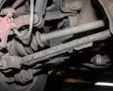 Widok od spodu na skorodowany wielowahacz z widoczną piastą, przegubem i elementami zawieszenia.