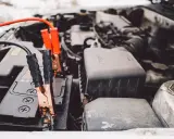 Kable rozruchowe podłączone do akumulatora, który wygląda na rozładowany. Czerwony i czarny kabel z klemami.