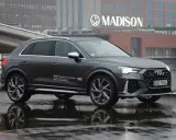 Szary Audi RS Q3 na mokrej nawierzchni, z odbiciem w kałuży. W tle budynek z napisem MADISON.
