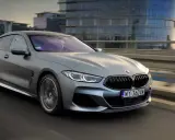 Srebrne BMW M850i sunie po moście, odbijając światła miasta w swoich lśniących szybach.