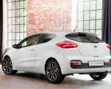 Biały Kia pro_ceed 1.6 CRDi z eleganckimi felgami stoi w stylowym wnętrzu z ceglaną ścianą i dużymi oknami.