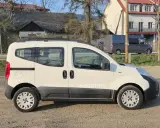 Biały Citroen Nemo z napisem "Autoline" stoi na żwirowej drodze. W tle widać domy i szare furgonetki.