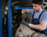 Mechanik w warsztacie pracuje nad adaptacją skrzyni biegów, używając klucza do dokręcenia śrub.