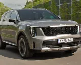 Nowa Kia Sorento w kolorze szarym, z charakterystycznym grillem i nowoczesnymi światłami, pędzi po drodze.