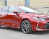 Błyszcząca, czerwona Toyota Corolla 1.8 Hybrid stoi na tle nowoczesnego budynku.