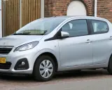 Srebrny Peugeot 108 stoi zaparkowany przed ceglanym domem.