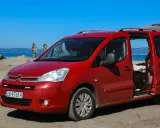 Czerwony Citroen Berlingo 1.6 HDI na plaży, z otwartymi drzwiami i bagażnikiem, na tle morza i palmy.