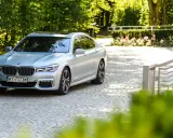 Srebrne BMW 750i lśni w słońcu na brukowanym podjeździe, otoczone zielenią i różami.