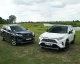 Dwa modele Toyota RAV4 2020, jeden czarny, drugi biały, stoją na trawie nad jeziorem.