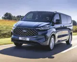 Ciemnoniebieski ford 7 osobowy Tourneo Custom pędzi po drodze wśród pól.
