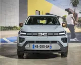 Jasnoszary dacia elektryk z miedzianymi lusterkami. Z przodu logo Dacia i tablica rejestracyjna MA-080-AM 92.