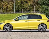 Żółty hatchback z przyciemnianymi szybami stoi na tle zieleni i drzew.