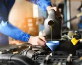 Mechanik w niebieskim kombinezonie nalewa olej do silnika przez lejek. Szybka wymiana oleju to klucz do sprawnego działania auta.