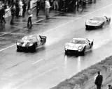 Trzy samochody Ford GT40 ścigają się po mokrym torze.