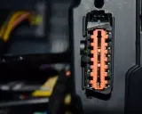 Pomarańczowe złącze elektryczne w samochodzie Mercedes B180, otoczone przewodami.