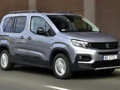 Szary Peugeot Rifter z relingami dachowymi jedzie po drodze. Kierowca w kabinie.