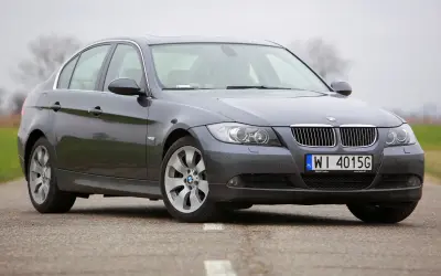 Szary sedan BMW E90 2.0 benzyna na drodze.