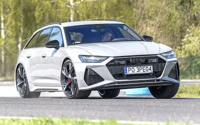 Białe Audi RS6 Avant na torze, kierowca wpatrzony przed siebie.