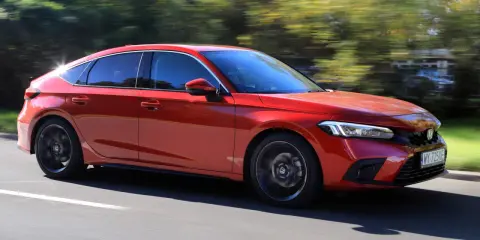 Czerwony Honda Civic 2025 pędzi po drodze, otoczony rozmazaną zielenią drzew.