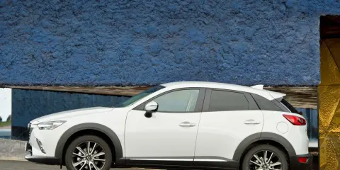 Biała Mazda CX-3 na tle niebieskiej ściany. Sprawdź aktualną mazda cx3 cena i wybierz swój wymarzony samochód.