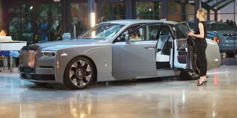 Elegancki szary Rolls-Royce Phantom z otwartymi drzwiami, obok którego stoi kobieta. Poznaj jego wyjątkową rolls royce phantom cena.