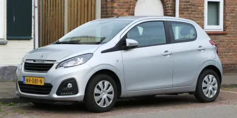 Srebrny Peugeot 108 stoi zaparkowany przed ceglanym domem.