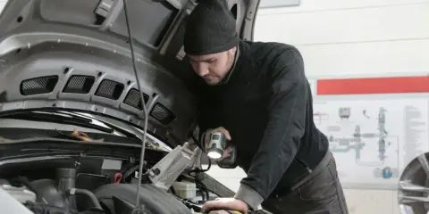 Mechanik z latarką bada silnik Renault, szukając przyczyny błędu DTC P0380.