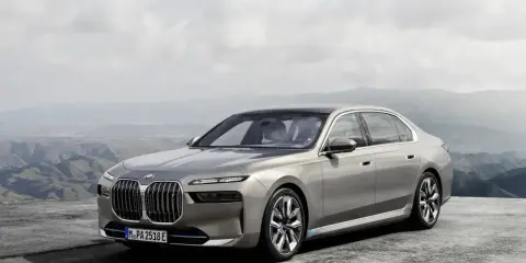 Eleganckie, srebrne BMW 7 2025 z niebieskimi akcentami na felgach, zaparkowane na tle górskiego krajobrazu.