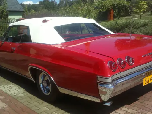 Czerwona kabrioletowa Chevy Impala z białym dachem, zaparkowana na podjeździe z kostki brukowej.