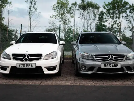 Dwa Mercedesy C63 AMG W204, biały i szary, stoją obok siebie na parkingu.