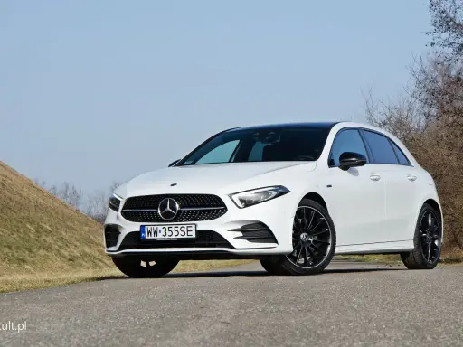 Biały Mercedes A250 z czarnym dachem i felgami stoi na drodze, na tle wzgórza i drzew.