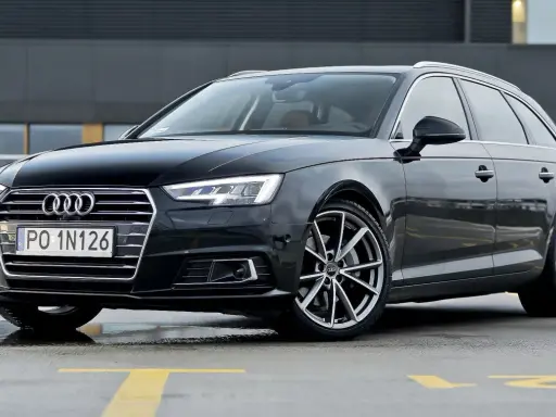 Czarny Audi A4 Avant, model b9, zaparkowany na mokrym parkingu z żółtymi liniami.