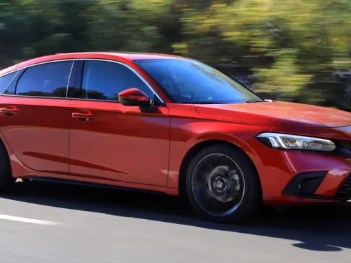 Czerwony Honda Civic 2025 pędzi po drodze, otoczony rozmazaną zielenią drzew.