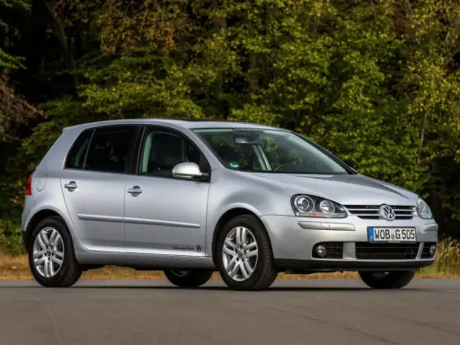 Srebrny Volkswagen Golf V stoi na drodze, otoczony zielenią drzew.