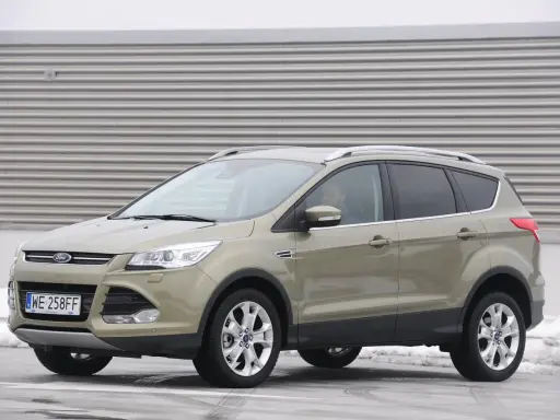 Złoty Ford Kuga 2.0 TDCI z polskimi tablicami WE 258FF zaparkowany na tle industrialnej ściany.