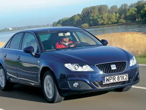 Granatowy Seat Exeo 2.0 TDI jedzie drogą nad rzeką, kierowca w czerwonej kurtce.
