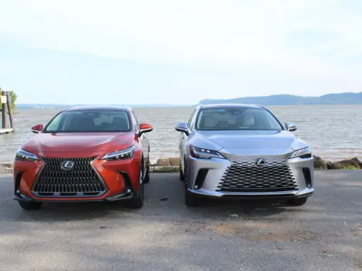 Dwa lśniące suvy Lexus stoją obok siebie nad wodą.