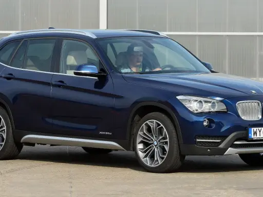 Ciemnoniebieskie BMW X1 E84 z kierowcą za kierownicą, zaparkowane na zewnątrz.