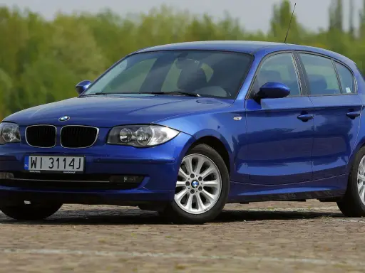 Niebieskie BMW 118i na tle zieleni. Elegancki hatchback z polskimi tablicami rejestracyjnymi WI 3114J.