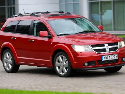 Czerwony Dodge Journey 3.6 z bagażnikiem dachowym jedzie po brukowanej drodze.