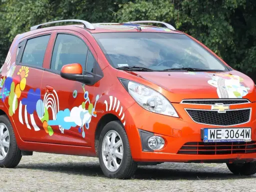 Pomarańczowy Chevrolet Spark z kolorowymi, abstrakcyjnymi wzorami na karoserii.
