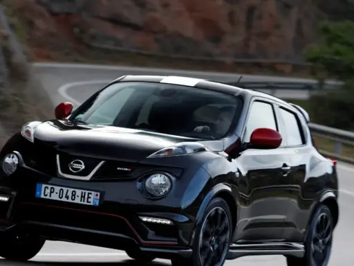 Czarny Nissan Juke Nismo z czerwonymi lusterkami i białym pasem na dachu pędzi po krętej drodze.
