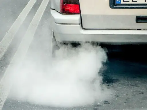 Z rury wydechowej wydobywa się gęsty, biały dym, tworząc chmurę na drodze.