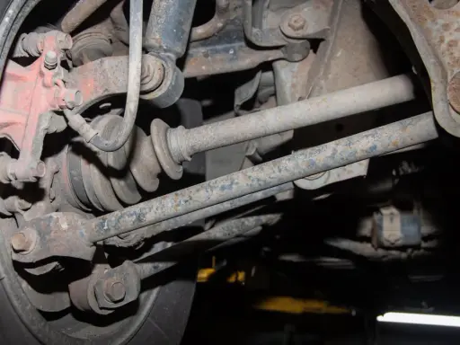 Widok od spodu na skorodowany wielowahacz z widoczną piastą, przegubem i elementami zawieszenia.