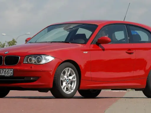 Czerwone BMW 116i z polskimi tablicami WI 3766G zaparkowane na czerwonym chodniku.